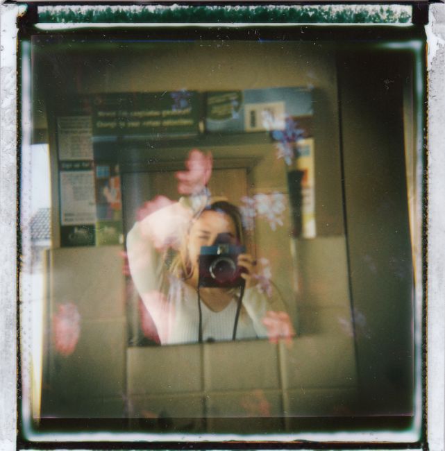 Artistic mirror selfie with floral overlay and analog camera effect, capturing a woman's reflection.