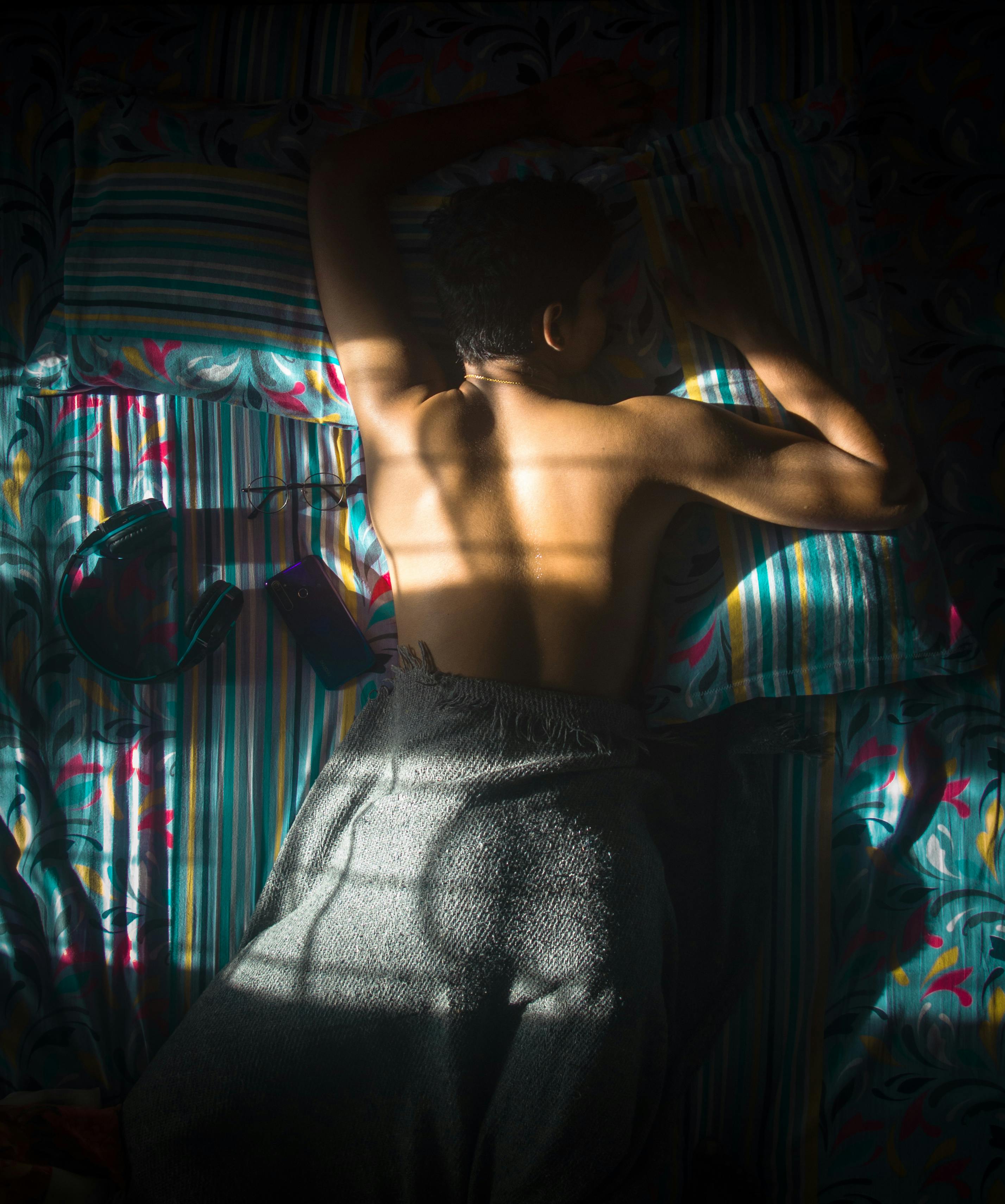 阳光明媚的卧室里，一个赤裸上身的男人躺在床上，营造出一种宁静的氛围