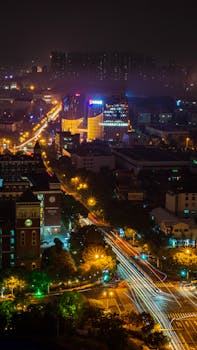 Aerial view of a lively cityscape at night, featuring illuminated streets and skyscrapers.