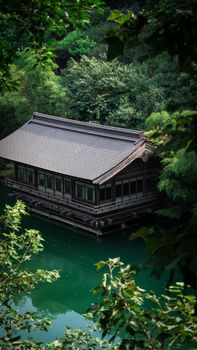 Traditional Japanese house surrounded by lush green forest by a serene water body.