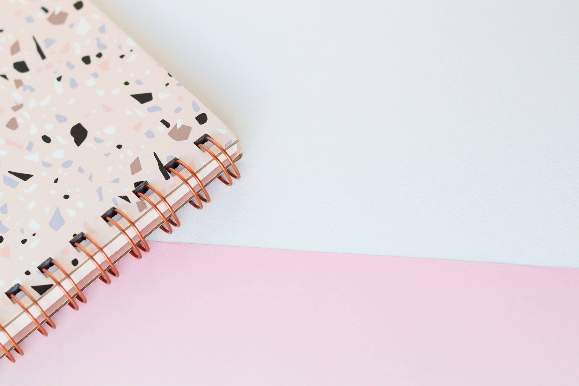 Elegant pink and white terrazzo notebook with spiral binding on a pastel colored desk.