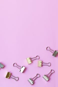 Overhead view of assorted binder clips on a vibrant pink surface with ample copy space.