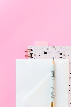 粉色背景上，信封、笔记本和铅笔平放着，非常适合创意项目
