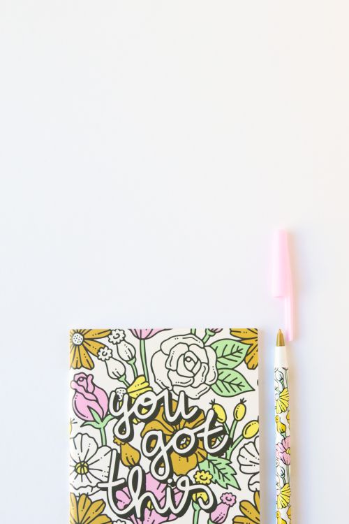 Free Flat lay of a floral notebook and pen with motivational text and ample copy space. Stock Photo