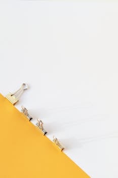 A minimalist photo of binder clips on a yellow and white background, perfect for office decor.