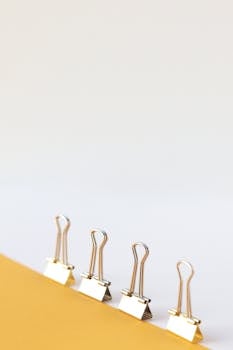 Minimalist arrangement of binder clips on a yellow surface with ample copyspace.