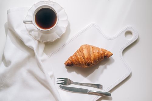Free Top view of a fresh croissant and black coffee served on a stylish white background with cutlery. Stock Photo