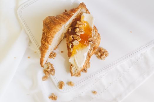 Delicious croissant with brie, apricot jam, and walnuts on a white plate.