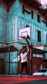 Young man playing basketball on an urban outdoor court at sunset.