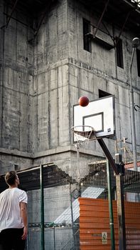 A man attempts a basketball shot in an urban setting against a concrete building backdrop.