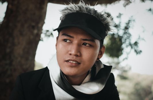 Portrait of a stylish young man with colored hair and hat in a natural outdoor setting.