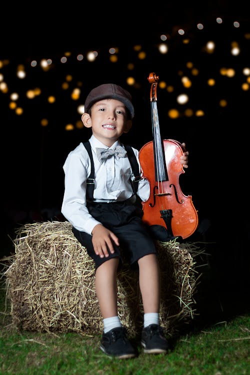 Boy Sitting on Hay While Holding a Violin