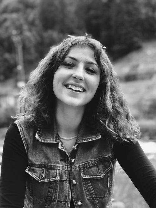 Free Captivating black and white portrait of a smiling woman in a denim vest in a natural setting. Stock Photo