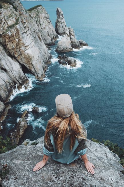 A woman sits on a cliff edge above the ocean, embracing adventure.