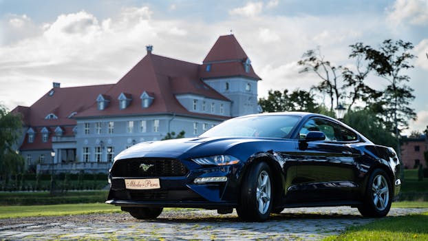 A sleek Ford Mustang parked in front of a historic mansion under a clear sky.