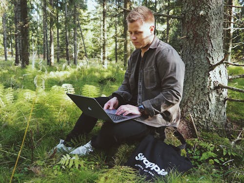 A Man Typing on His Laptop While in the Forest 