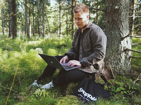 Man using a laptop while sitting in a lush Helsinki forest.