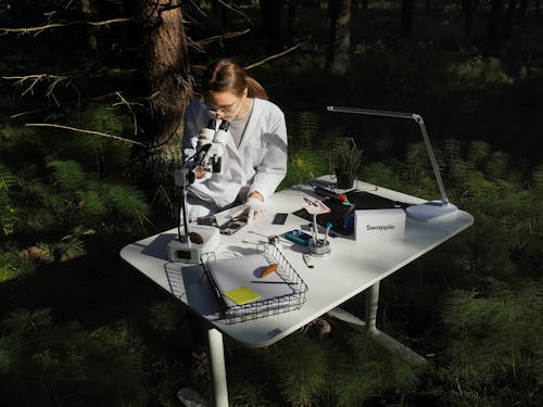 Woman Sitting Behind a Desk and Looking Through a Microscope Outdoors 