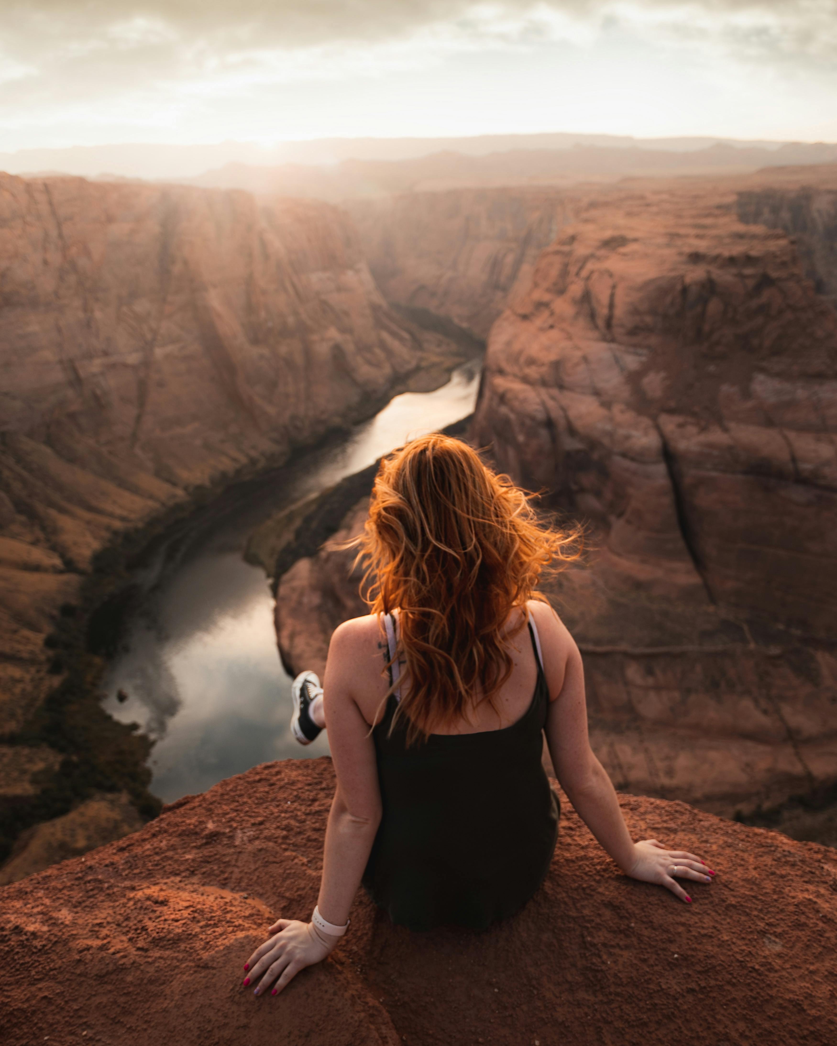 back view of a woman sitting on the cliff overlooking the canyon scenery