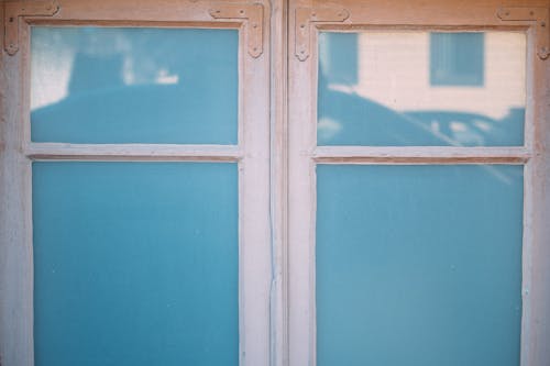 From outside view of closed window with white frame and blue glass reflecting street