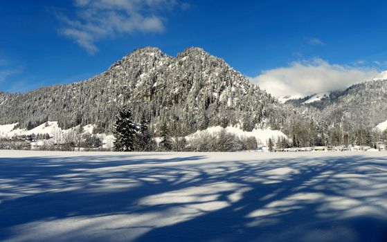 Captivating winter scene of snow-covered mountains and forest in Walchsee, Tirol, Austria under a clear blue sky.