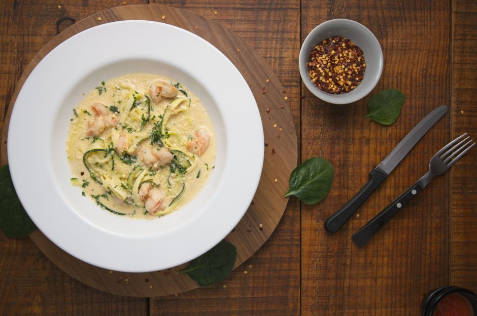 A skillet of spiralized zucchini noodles tossed with garlic butter shrimp, halved cherry tomatoes, grated parmesan, and torn basil leaves.