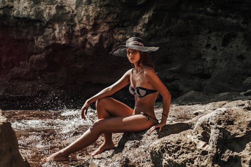 A Woman  Posing in Black Bikini Sitting on a Rock