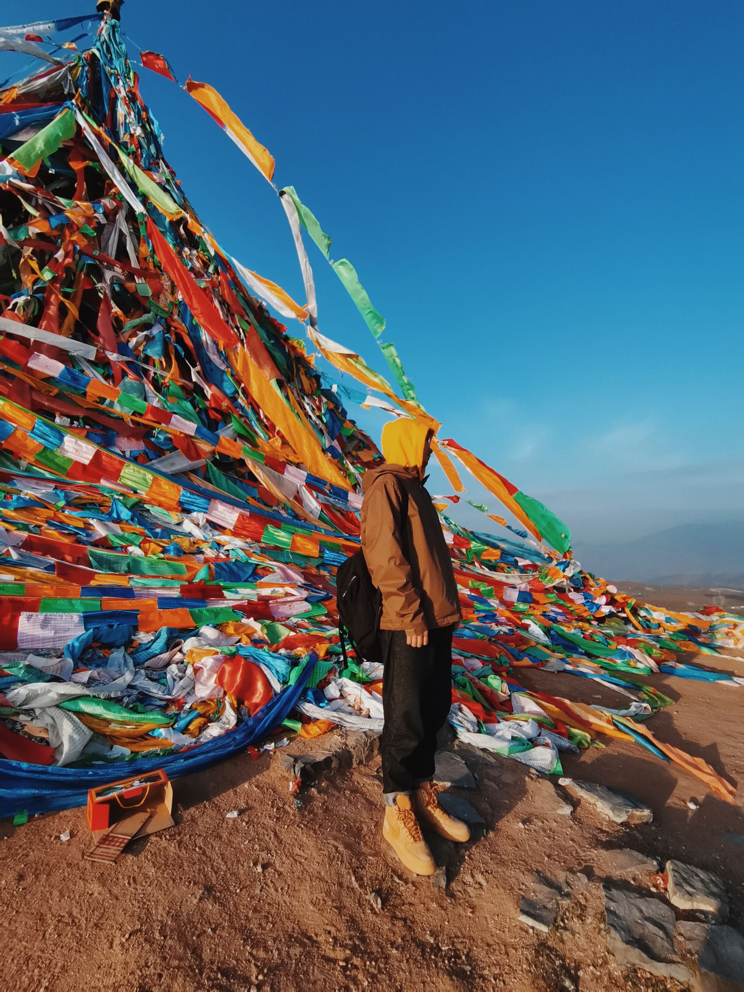 Person in Brown Jacket With Backpack Standing Near Prayer Flags With ...