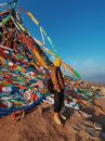 Person in Brown Jacket With Backpack Standing Near Prayer Flags With Mantra