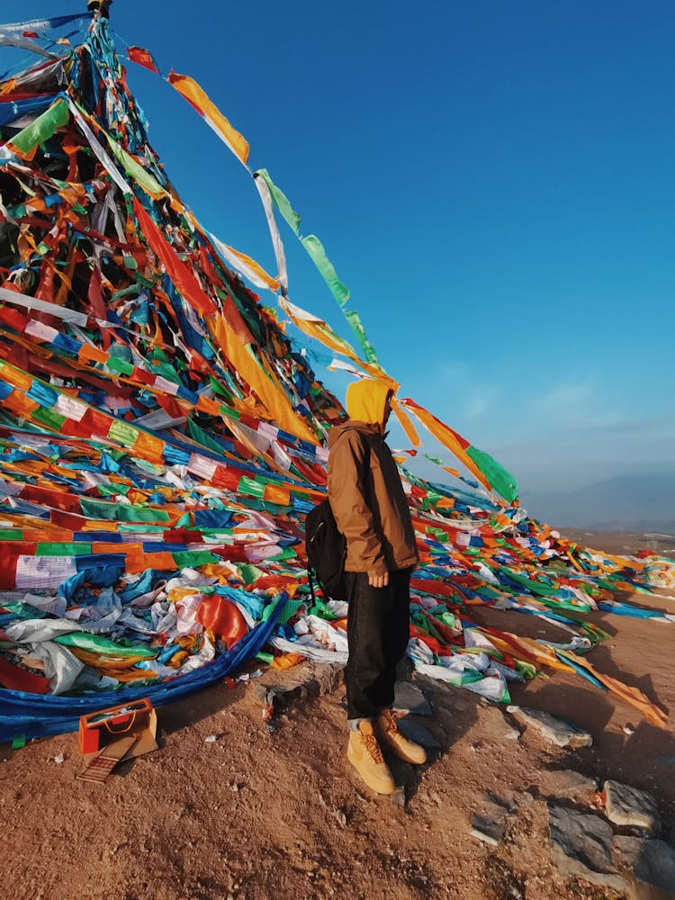 Person In Brown Jacket With Backpack Standing Near Prayer Flags With Mantra 