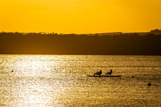 Silhouette of two kayakers gliding on Brazil's water against a golden sunset backdrop.