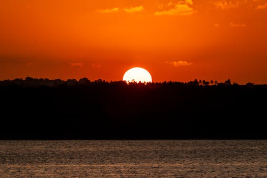 Stunning sunset over Brazilian waters with a vibrant red sky and silhouettes on the horizon.