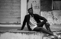 Black and white of serious black male in stylish clothes sitting on concrete stairs against old building with scuffed walls