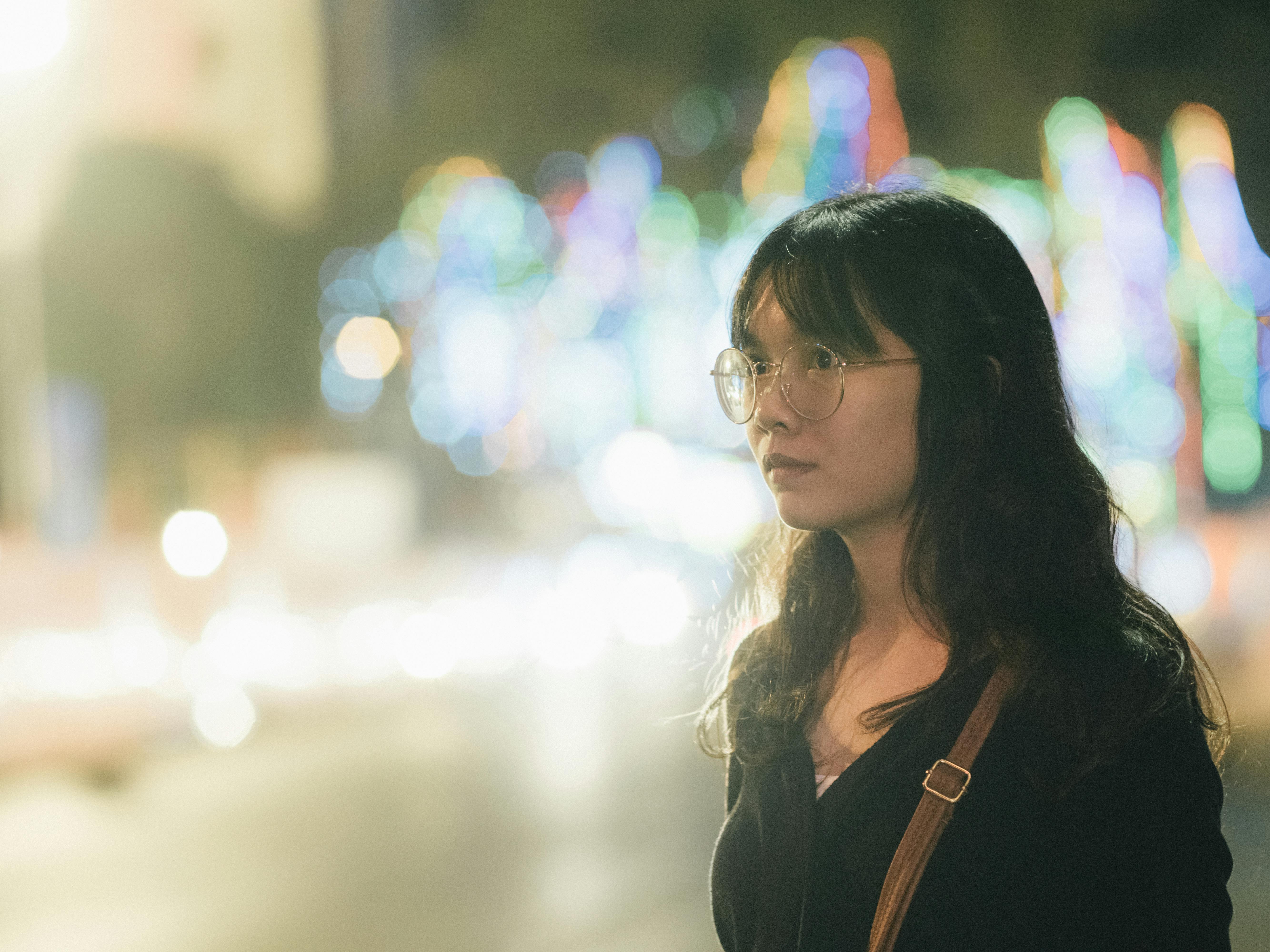 一位年轻女子戴着眼镜，站在五颜六色的城市灯光前，展现出充满活力的夜生活氛围