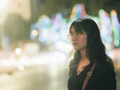 一位年轻女子戴着眼镜，站在五颜六色的城市灯光前，展现出充满活力的夜生活氛围