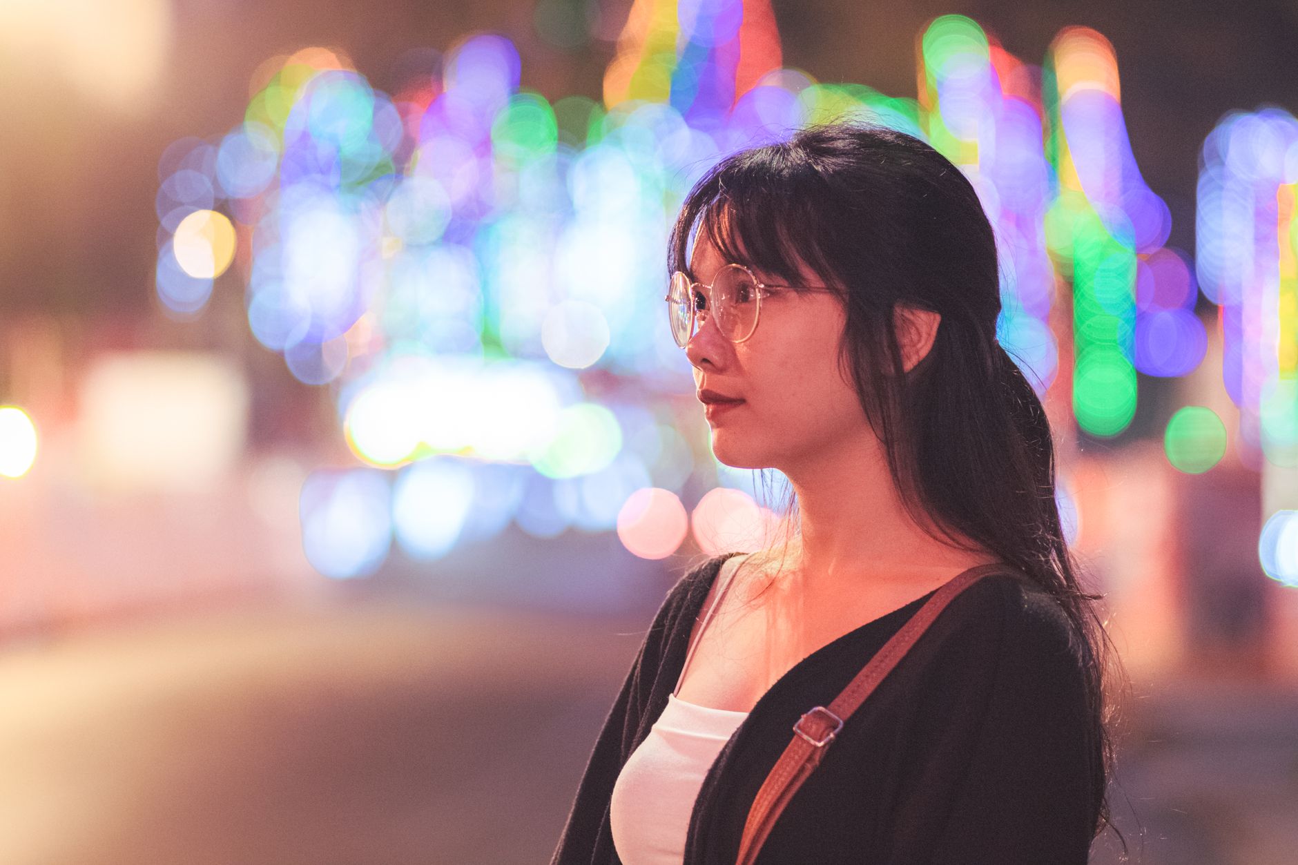 Profile of a woman with eyeglasses against colorful blurred city lights at night.
