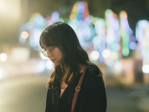 Free A young woman with glasses standing outdoors at night with colorful bokeh lights in Hà Giang, Vietnam. Stock Photo
