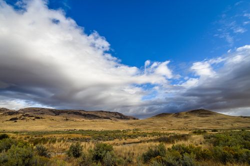 Free Landscape of dry meadow grass and shrubs growing in terrain against rocky hills under cloudy sky Stock Photo