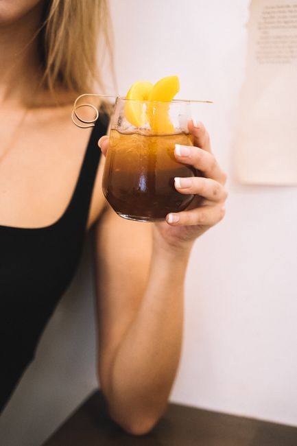 A tall glass of iced peach tea with peach slices and a mint sprig, condensation beading on the outside of the glass on a wooden table.