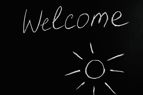 Free Chalk-drawn 'Welcome' and sun illustration on a black chalkboard background. Stock Photo