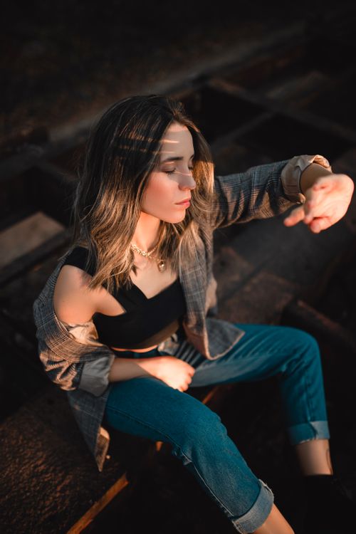 Free A young woman with closed eyes in soft sunlight, dressed casually and sitting outdoors in a peaceful setting. Stock Photo