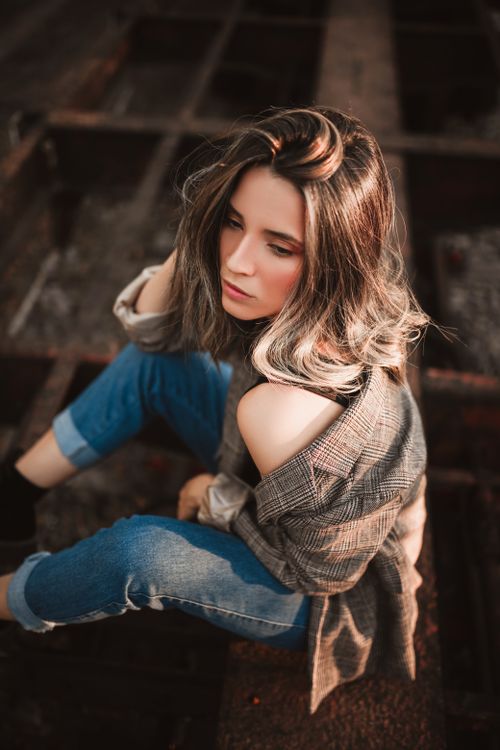 Free A fashionable woman with shoulder-length hair sits outdoors on a rustic surface. Stock Photo