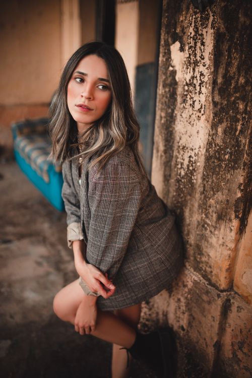 Free A young woman poses in a plaid blazer against a rustic background, exuding a fashionable and thoughtful vibe. Stock Photo