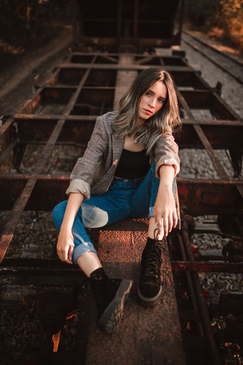 Free A fashionable woman sits on an old train track, exuding confidence and style. Perfect for lifestyle themes. Stock Photo
