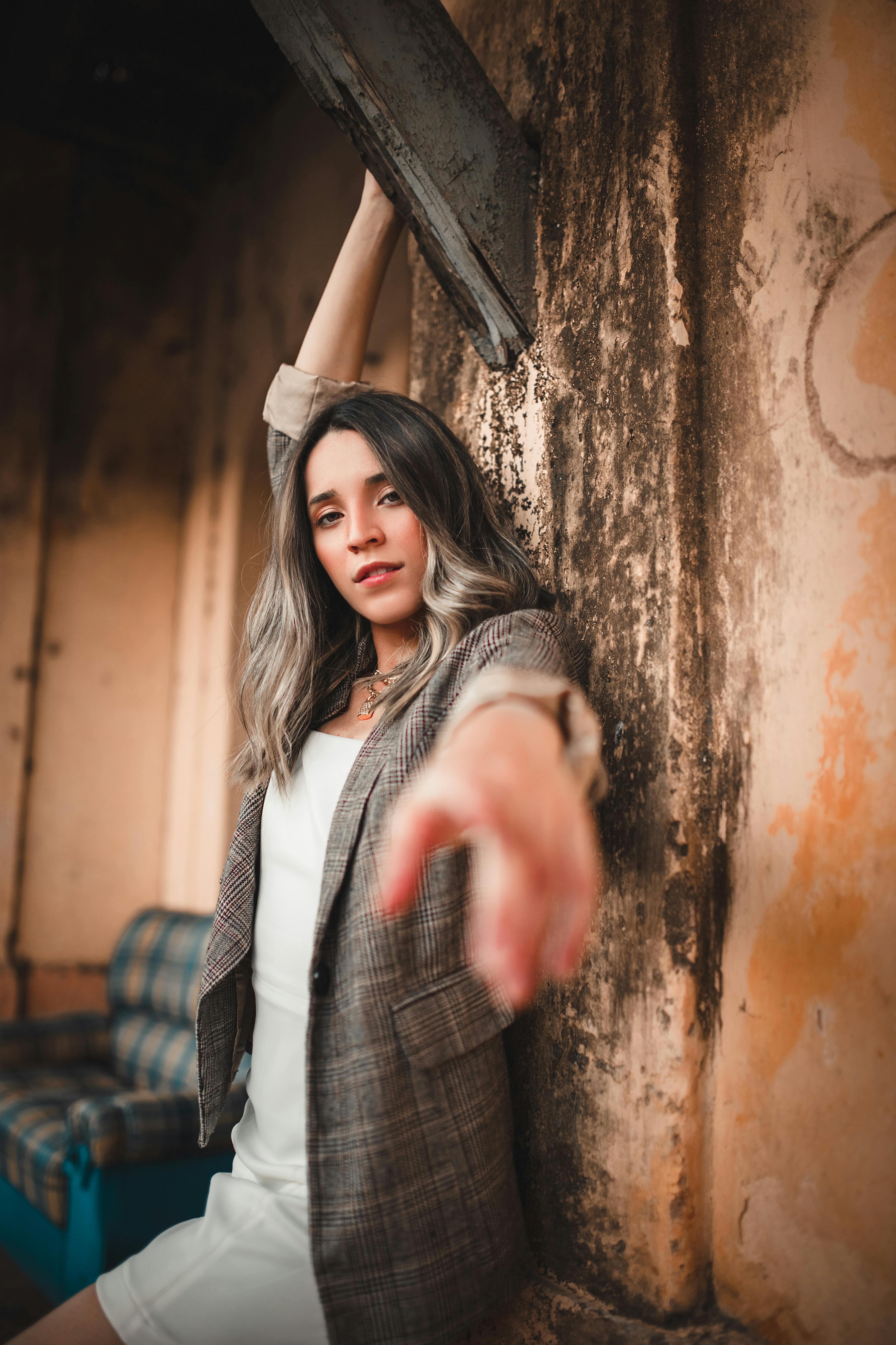 Fashionable woman in a plaid coat posing confidently against a rustic wall outdoors.