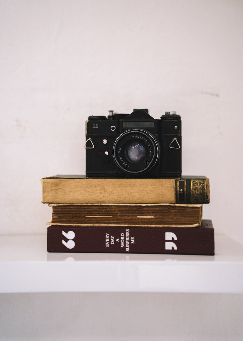 An antique film camera rests atop a stack of books, creating a classic still life scene.