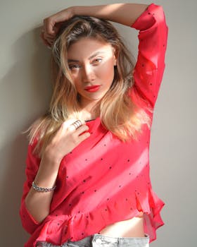 Beautiful woman posing with hand on head, wearing a vibrant red blouse.