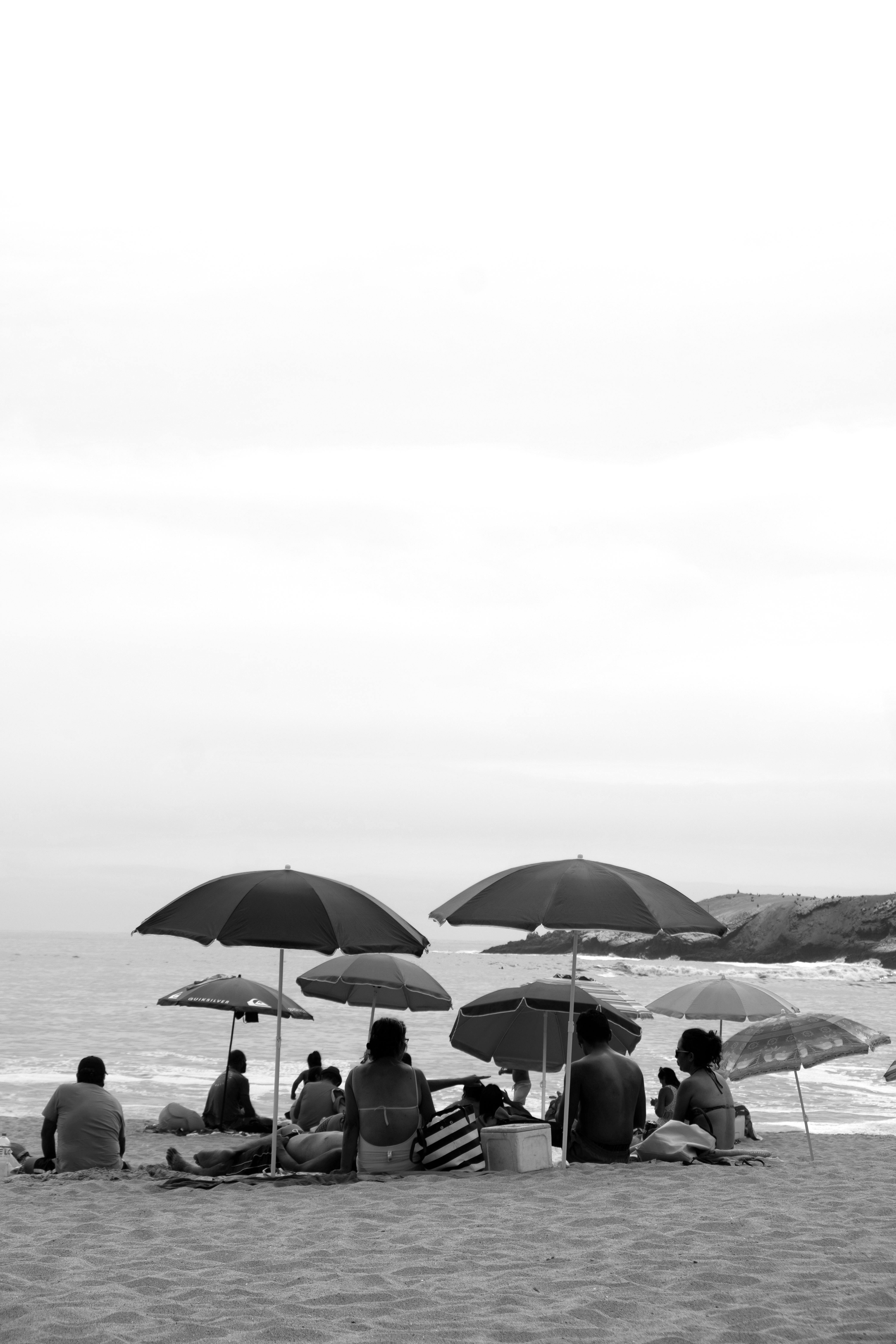 Black and white photo of people relaxing under umbrellas at a beach in Lima, Peru.