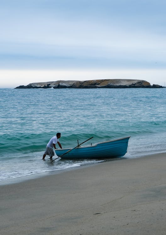 Man Standing with  Blue Boat on Beach