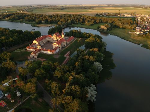 Free Explore the scenic aerial view of Niaśviž Castle in Belarus, surrounded by lush greenery and a serene river. Stock Photo